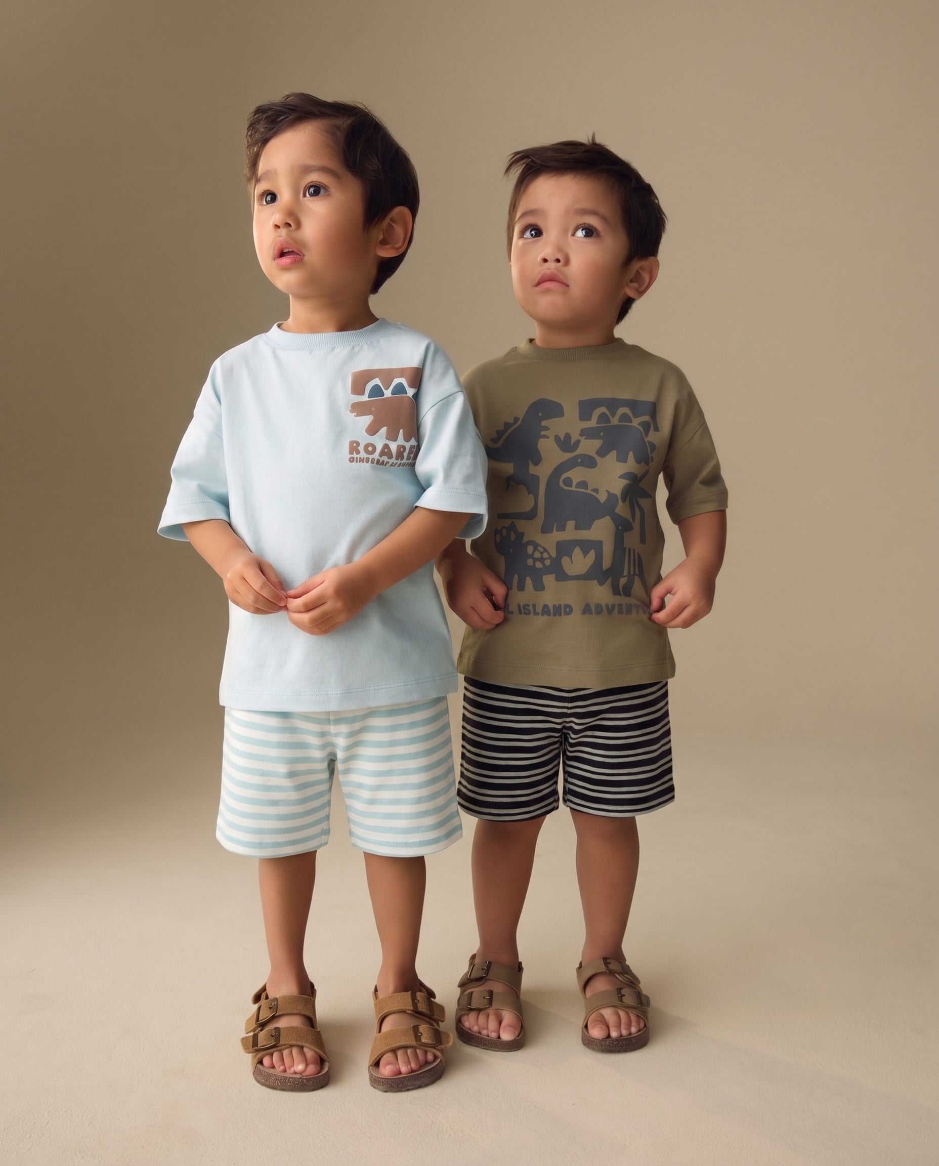 Two young boys wearing graphic t-shirts and stripe shorts on a beige background from PTex Fashion.