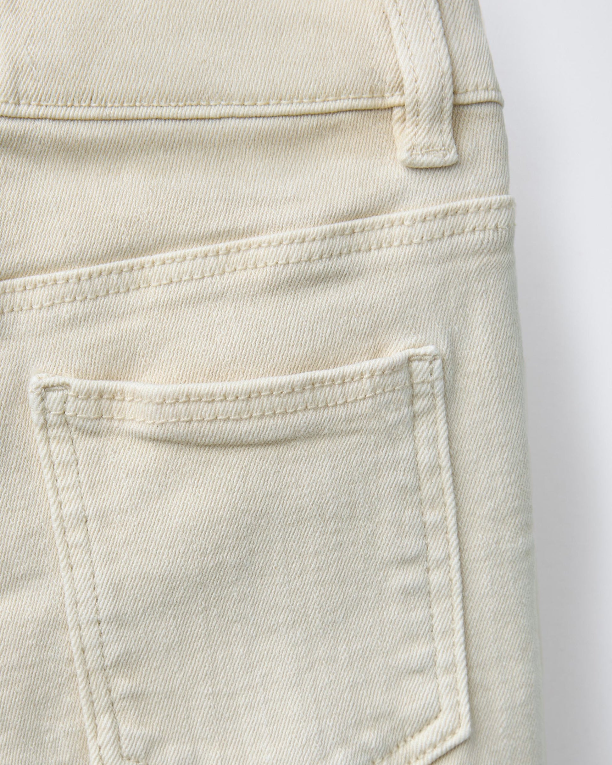 Close-up of back patch pocket on ecru cream boys' denim Bermuda shorts, showing tonal topstitching detail and soft natural cotton denim texture.