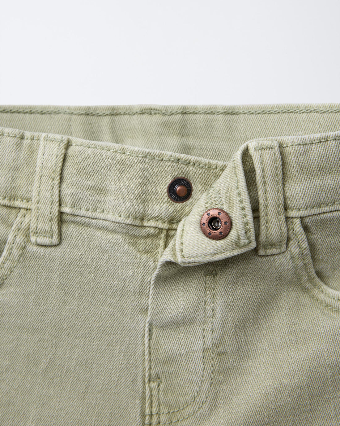 Sage green denim Bermuda shorts for boys, front view showing five-pocket styling, copper-tone shank button, zip fly, and belt loops on washed sage cotton denim.