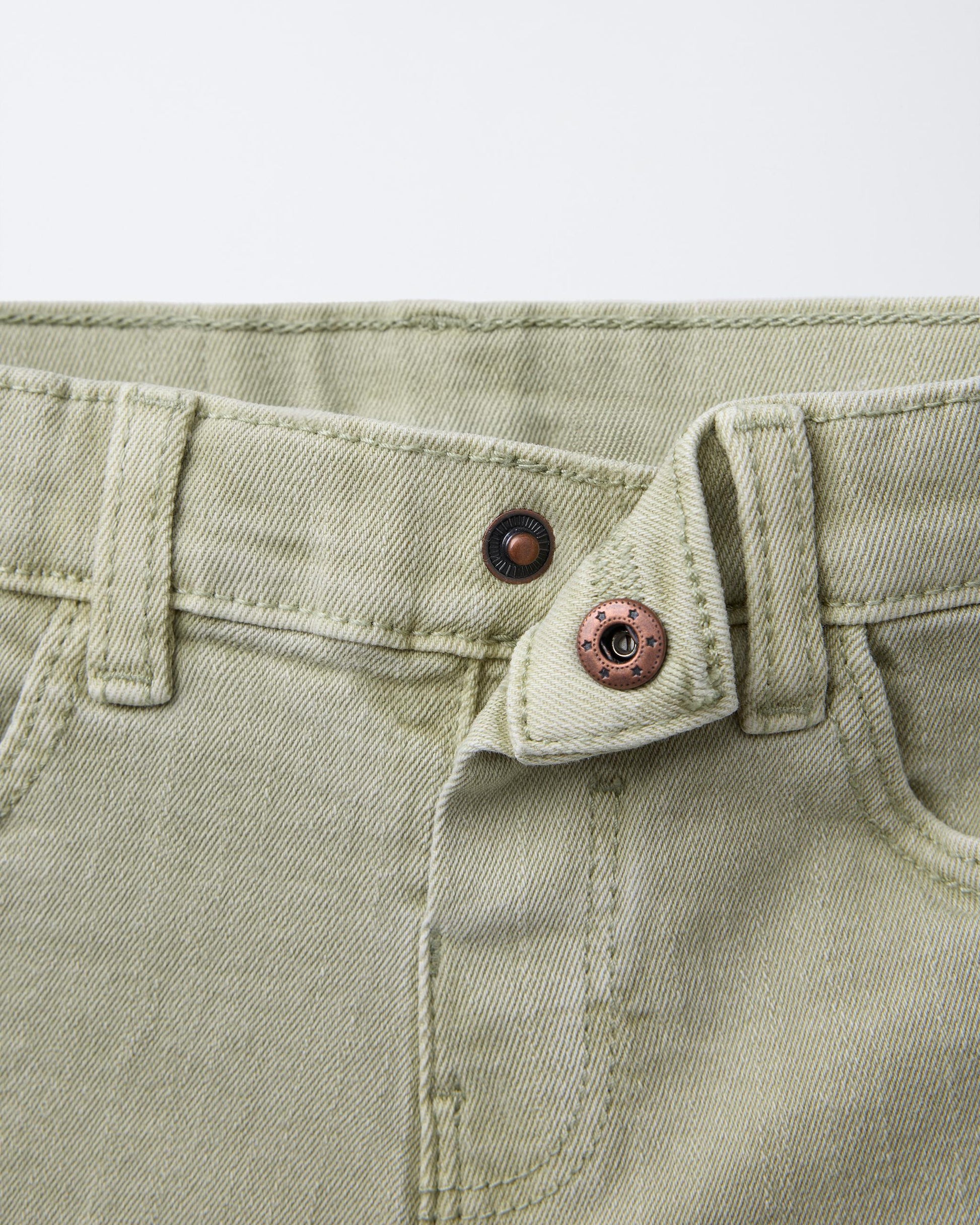 Detailed view of waistband, belt loops, and copper star-embossed shank button on sage green boys' denim Bermuda shorts, highlighting authentic denim hardware and clean stitching.