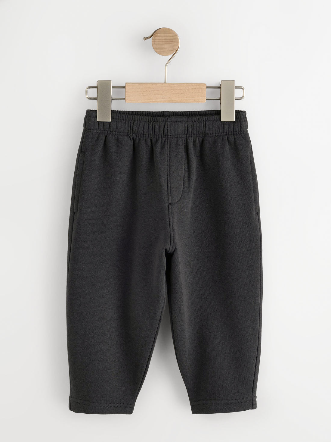 Black fleece joggers with elastic waist and side pockets on a wooden hanger - PTex Fashion