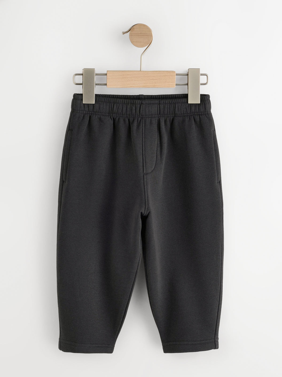 Black fleece joggers with elastic waist and side pockets on a wooden hanger - PTex Fashion