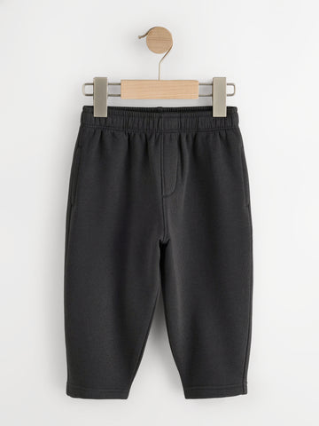 Black fleece joggers with elastic waist and side pockets on a wooden hanger - PTex Fashion