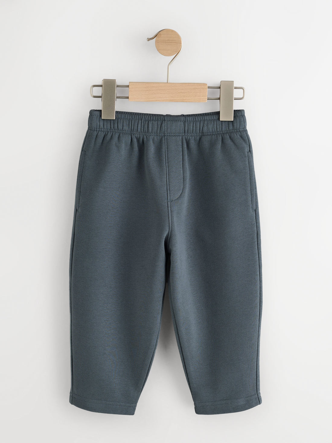 Slate blue fleece joggers with elastic waist and side pockets on a wooden hanger - PTex Fashion
