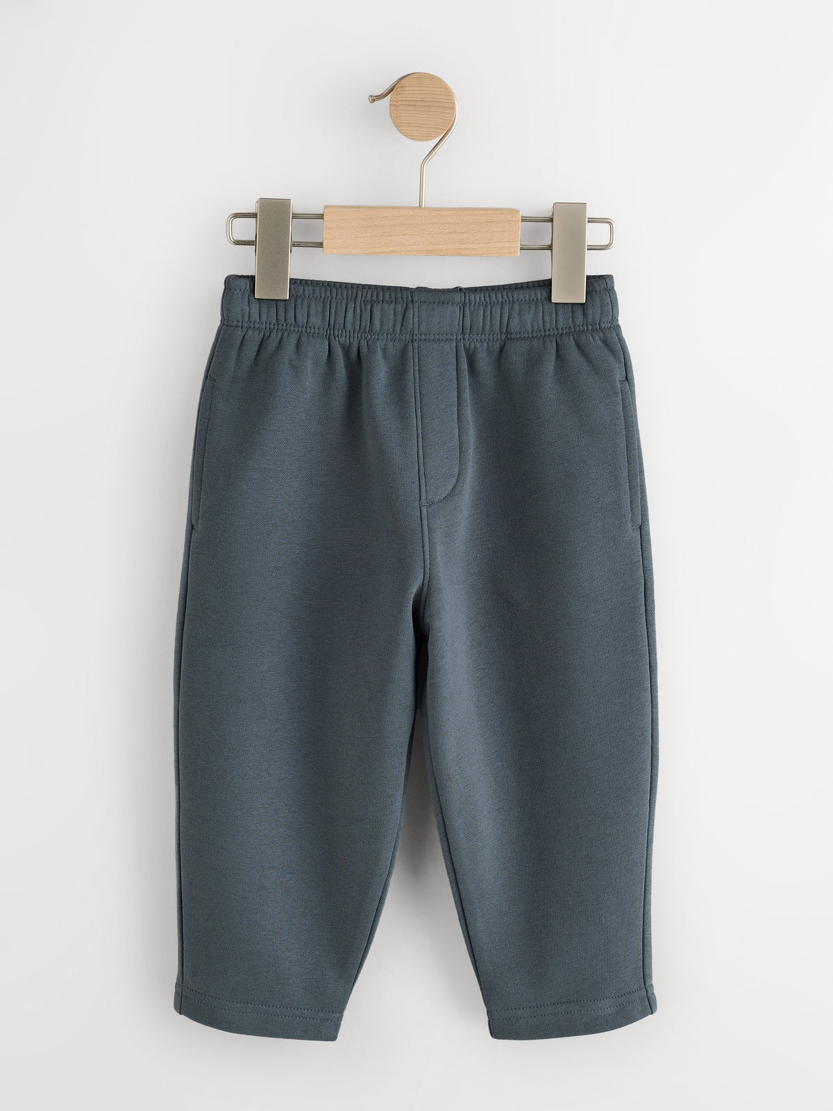 Slate blue fleece joggers with elastic waist and side pockets on a wooden hanger - PTex Fashion