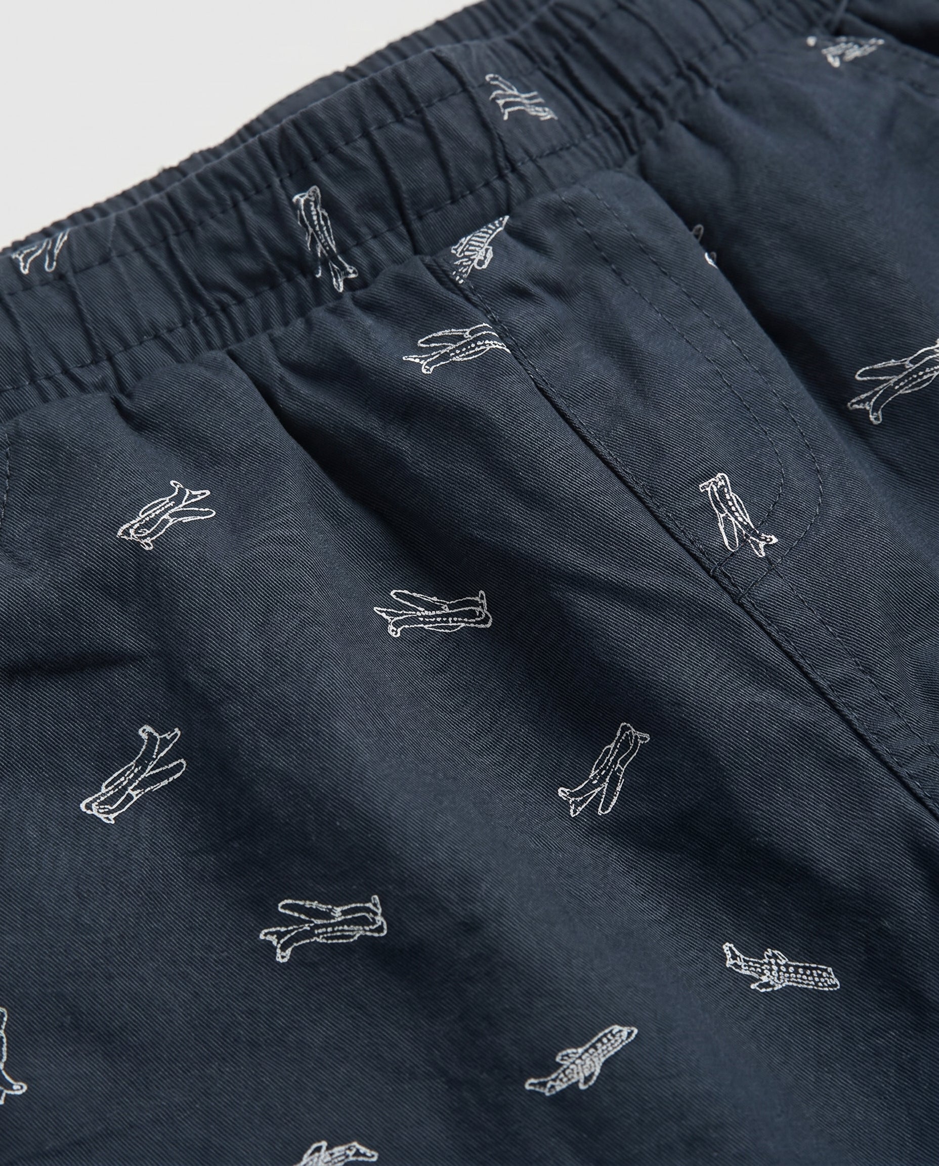 Close-up of navy blue cotton twill fabric with white airplane print and elastic waistband detail on boys' shorts