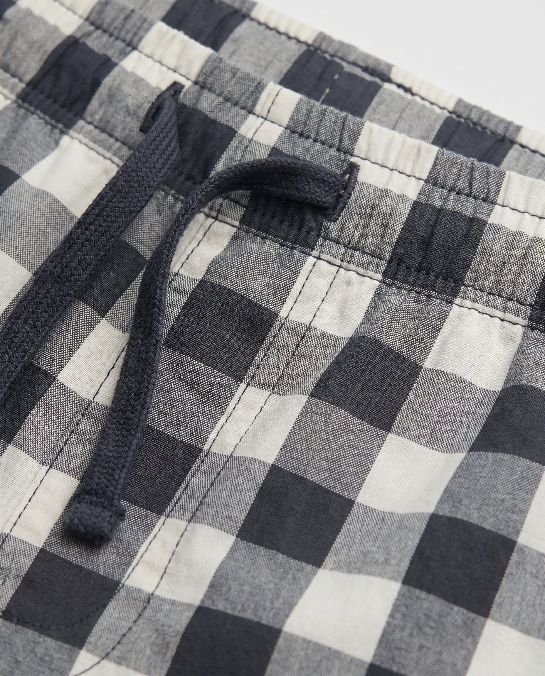 Close-up of boys' woven cotton short pant waistband showing navy drawstring and elasticated detail on navy and off-white oversized check fabric