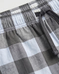 Close-up of boys' woven cotton short pant waistband showing elasticated drawstring detail in charcoal grey and light blue oversized check fabric