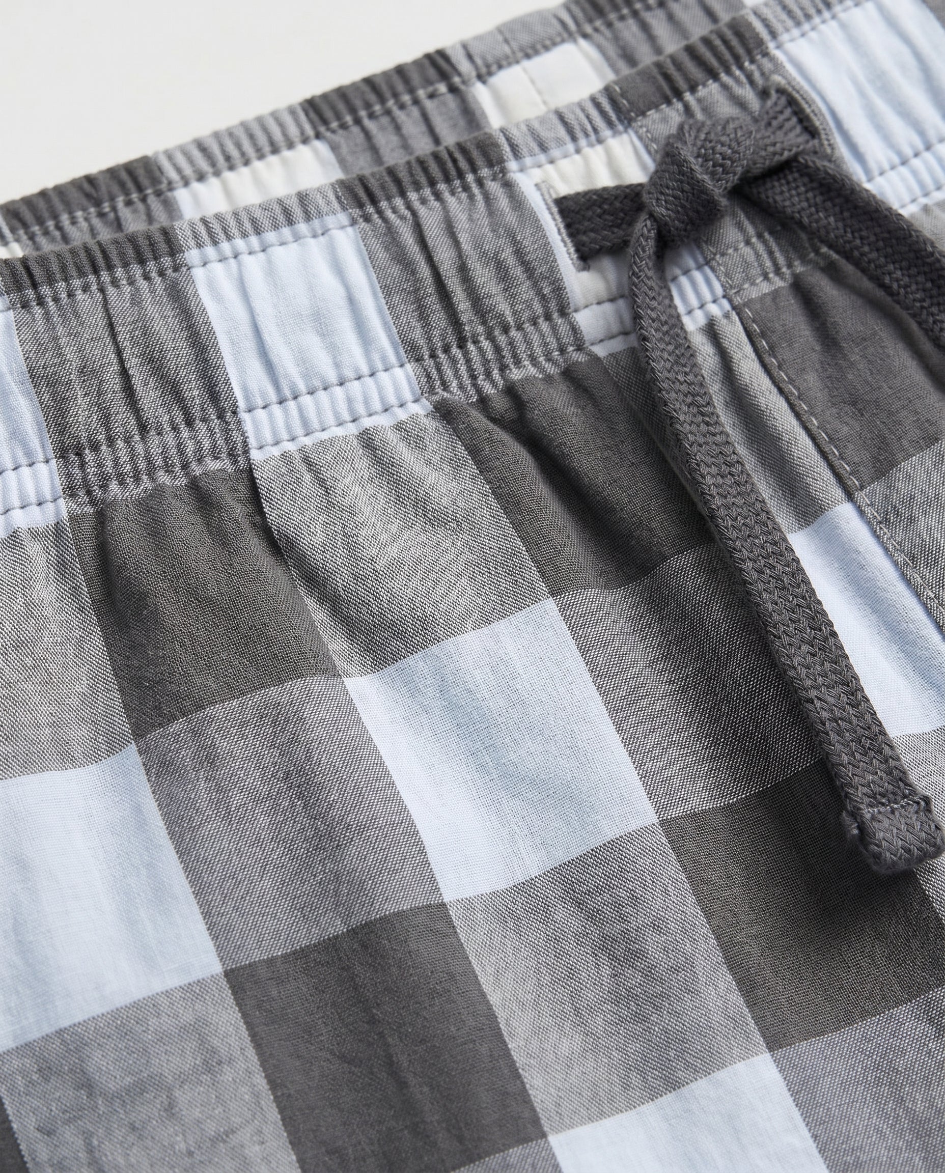 Close-up of boys' woven cotton short pant waistband showing elasticated drawstring detail in charcoal grey and light blue oversized check fabric