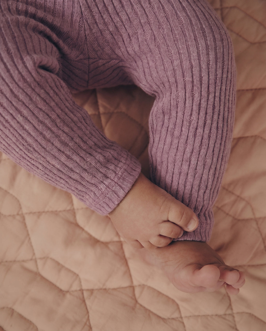 Baby girls' cable-knit leggings 3-pack in cream, blush pink, and mauve purple, flat lay on grey background