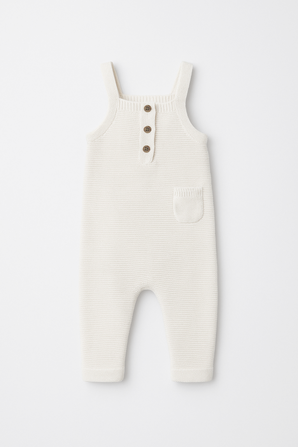 White ribbed knit overalls with button details on a light gray background