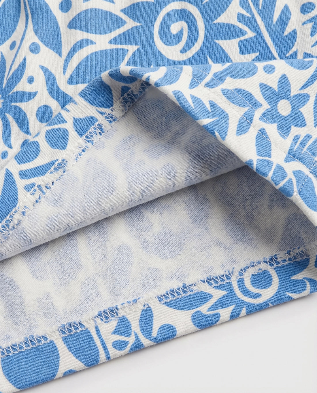 Front flat-lay view of girl's white short pant with all-over blue botanical folk floral print and ruched paperbag elasticated waistband