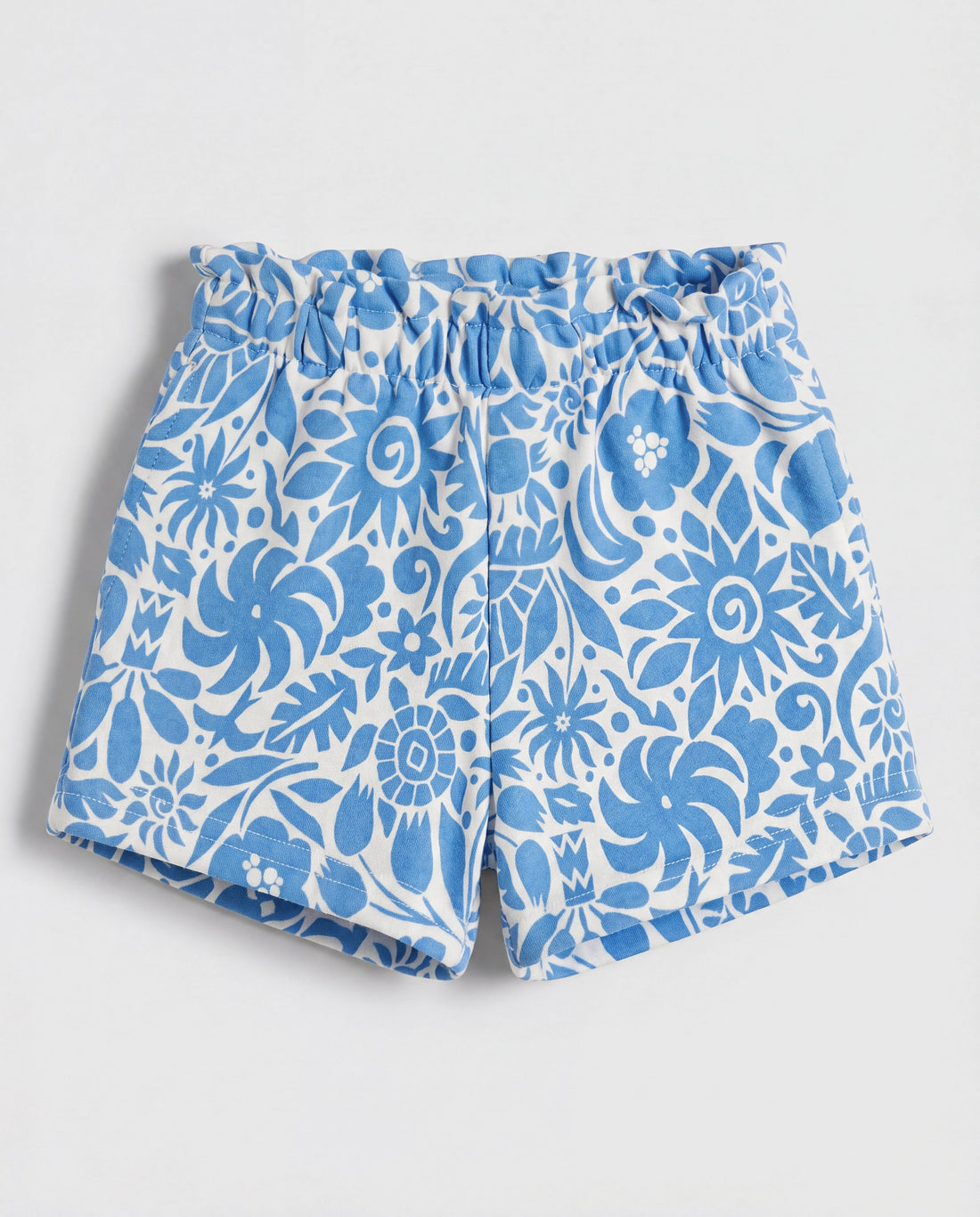 Front flat-lay view of girl's white short pant with all-over blue botanical folk floral print and ruched paperbag elasticated waistband