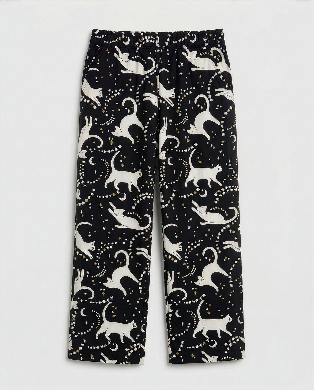 Girls' straight-cut wide-leg palazzo pants in deep black woven cotton with all-over celestial cat print — ivory white cat silhouettes in playful poses surrounded by gold and white star clusters and crescent moons, featuring full elastic waistband, flat-lay product photography on white background