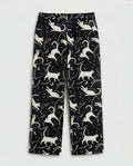Girls' straight-cut wide-leg palazzo pants in deep black woven cotton with all-over celestial cat print — ivory white cat silhouettes in playful poses surrounded by gold and white star clusters and crescent moons, featuring full elastic waistband, flat-lay product photography on white background