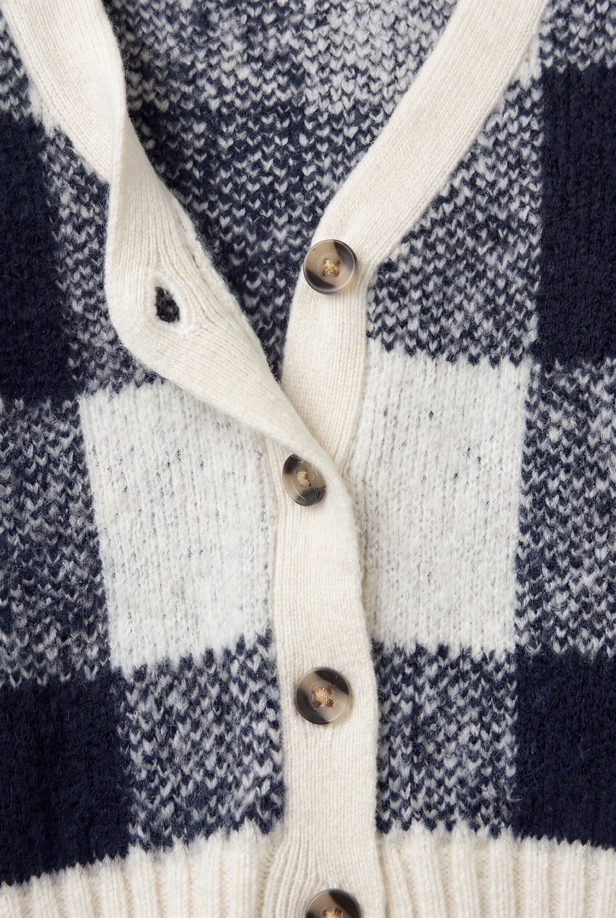 Close-up of PTex Fashion navy and ecru check knit cardigan showing ribbed button band, buttonhole and tortoiseshell-effect buttons