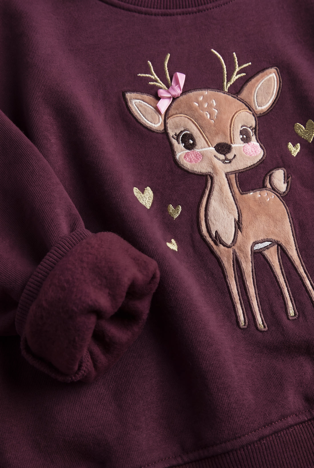 Girls wearing a boxy fit fleece sweatshirt with drop shoulders and embroidered deer appliqué design.