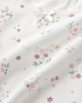 Close-up of white cotton fabric with scattered ditsy floral print in pink and sage, satin bow and lace trim detail on girls tank top