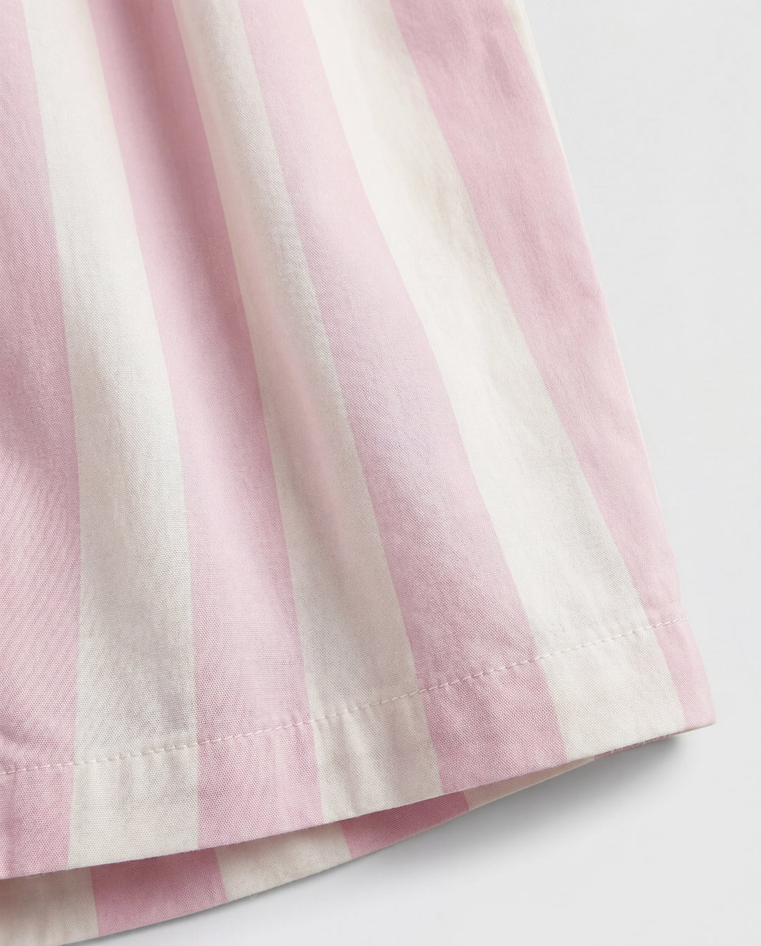 Close-up leg detail:
Close-up of girls' straight-cut palazzo pant leg panel showing bold blush pink and off-white vertical stripe woven cotton fabric with soft natural folds and clean single-needle hemline stitching.
