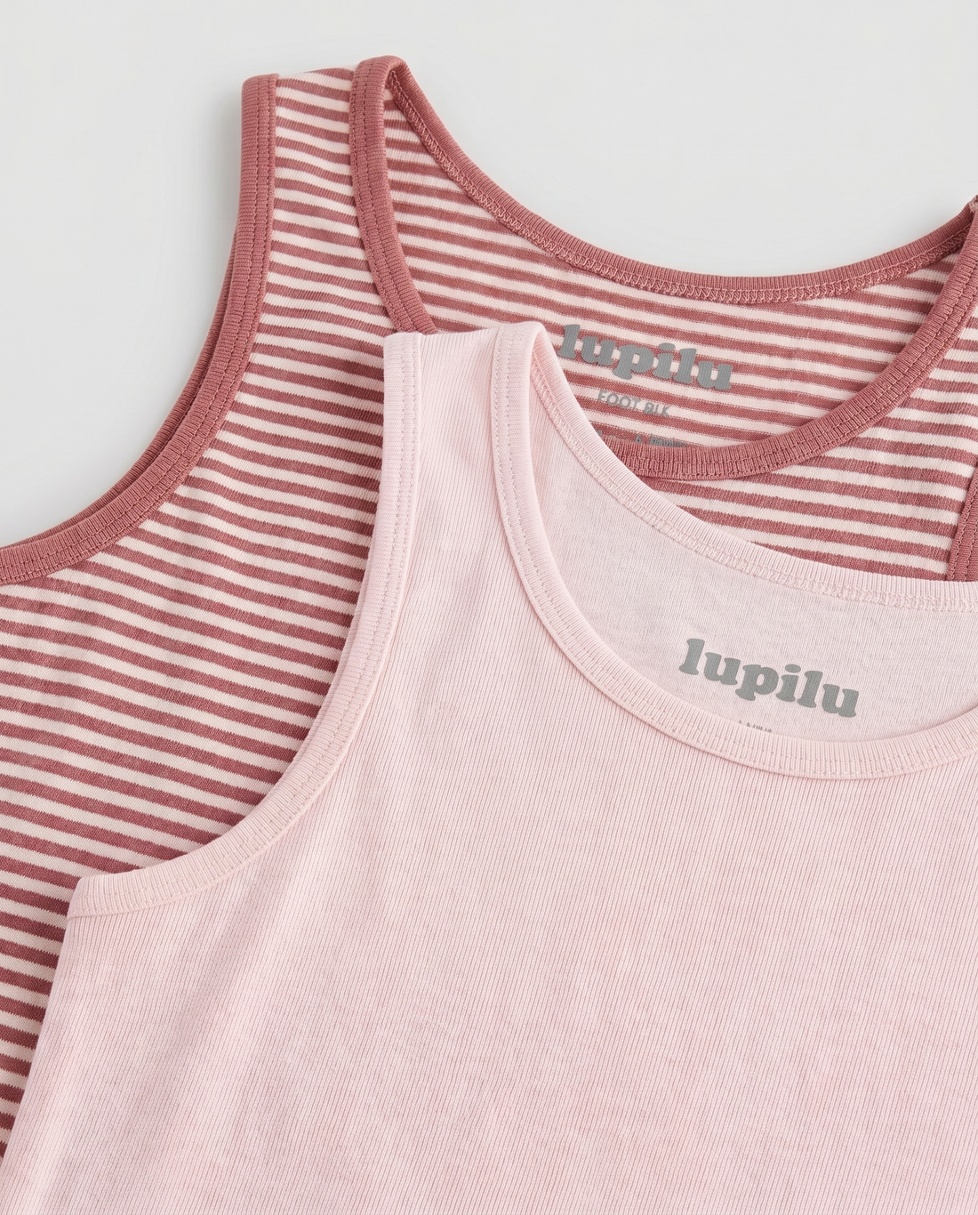girls' 2-pack cotton tank top set displayed flat on a white background — solid soft pink scoop-neck tank on the left and rose-and-cream horizontal striped tank with contrast binding on the right, showing full silhouette and length.