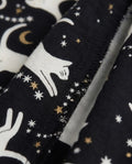 Extreme close-up of girls' black woven cotton palazzo pants showing inner leg seam with serged overlock stitching finish, fabric texture detail, and celestial cat print with white cat silhouettes, gold stars, and crescent moon motifs on black cotton