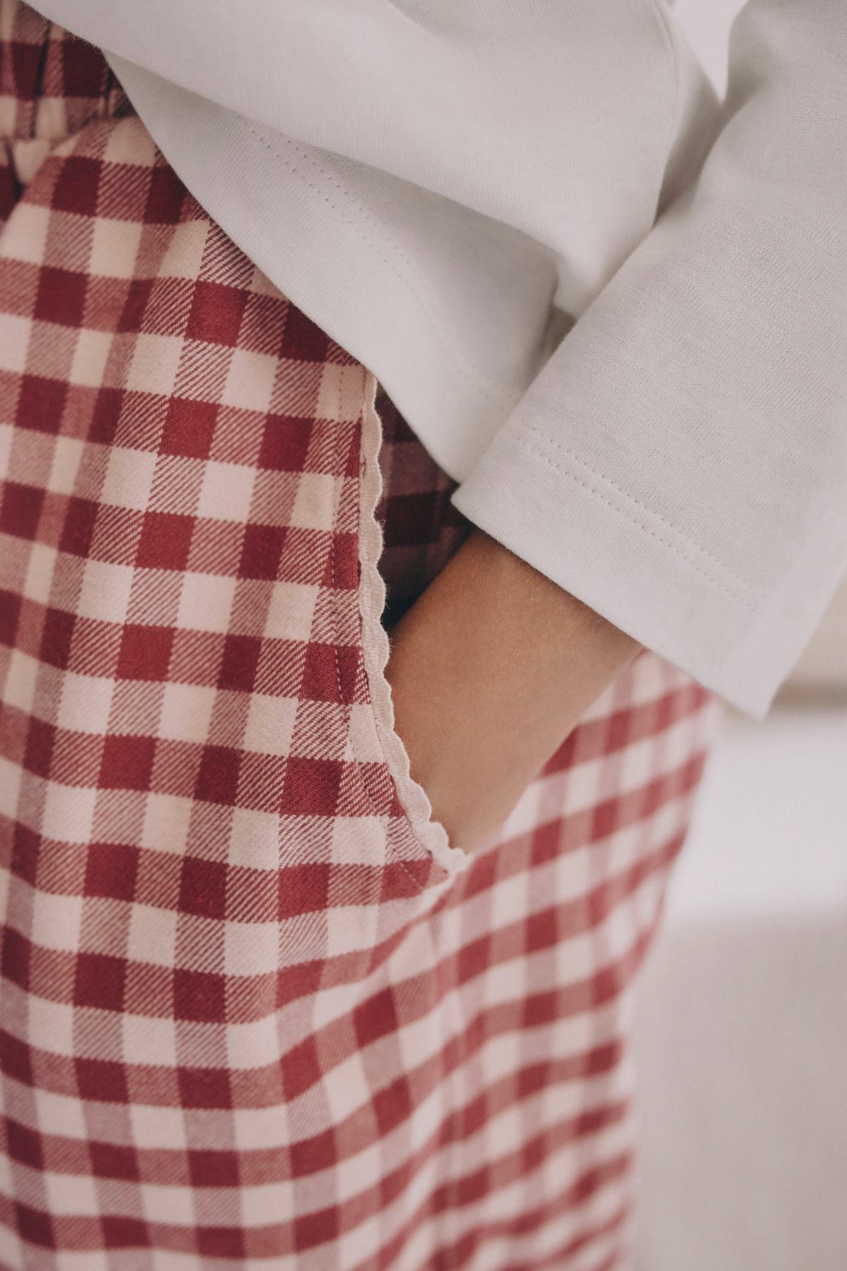 On-model pocket detail: PTex Fashion girls' berry gingham cotton trousers, hand in scalloped trim side pocket