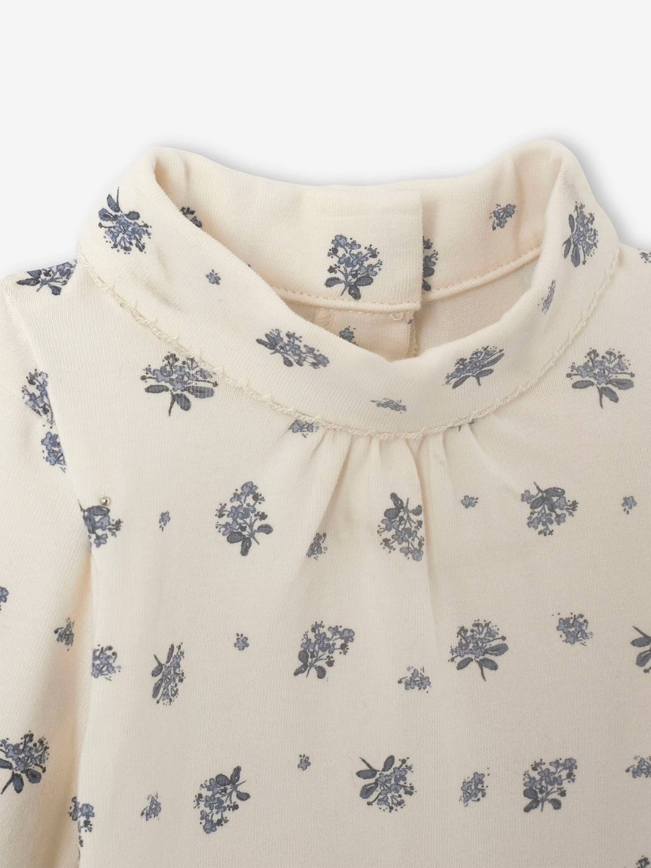 Close-up of a cream-colored blouse with blue floral patterns on a white background
