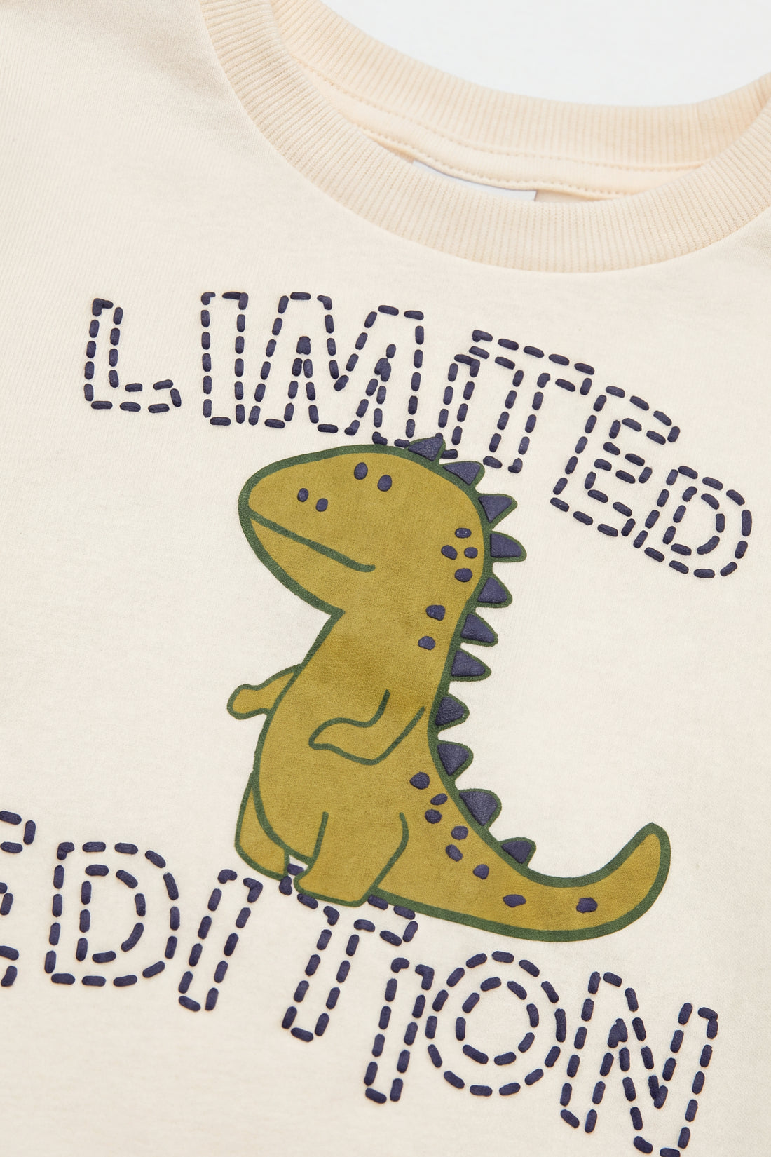 PTex Fashion kids’ two-piece set with a cream crew-neck sweatshirt featuring a dinosaur graphic and navy joggers with ribbed ankle cuffs, flat lay