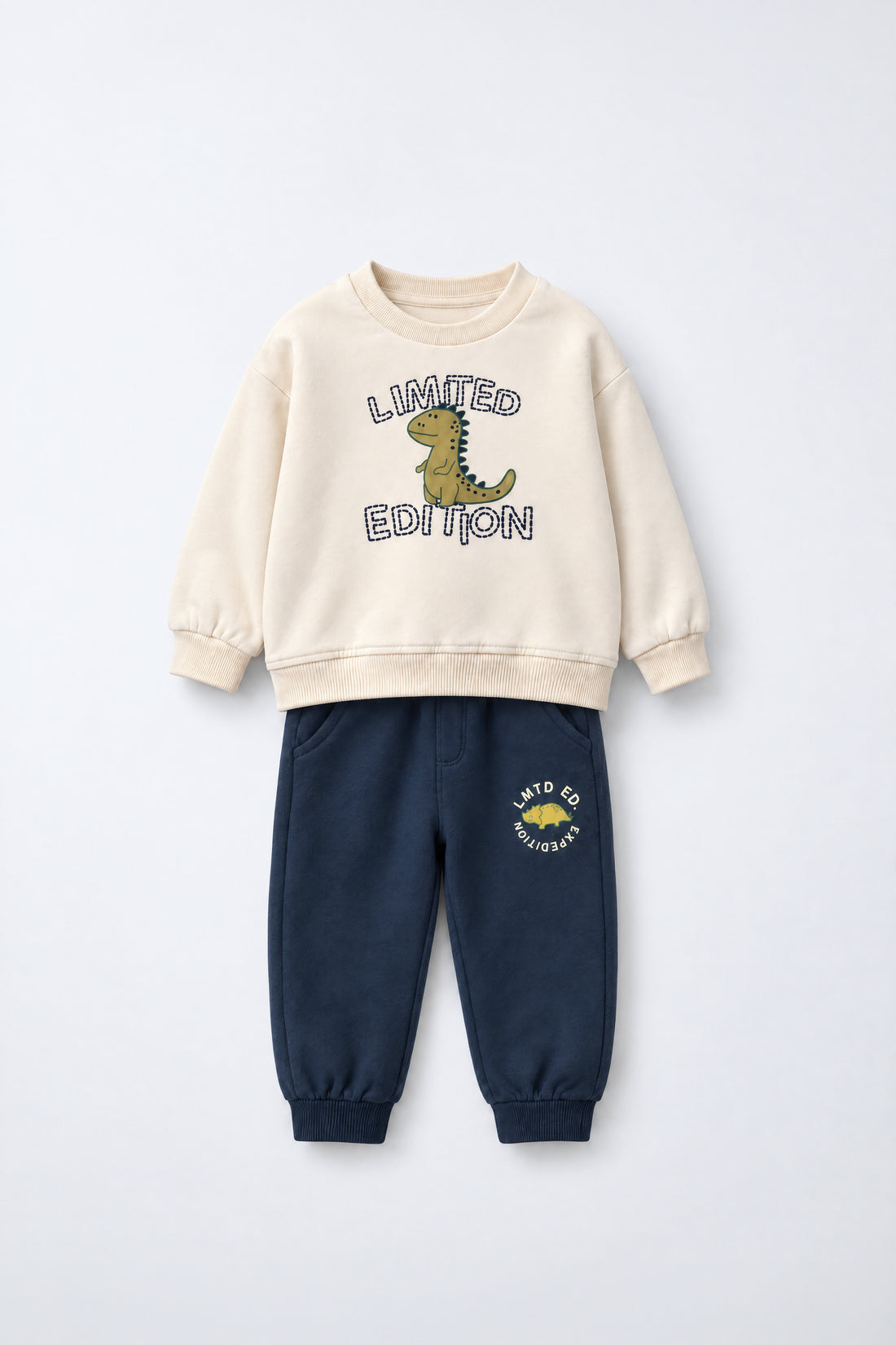 PTex Fashion kids’ two-piece set with a cream crew-neck sweatshirt featuring a dinosaur graphic and navy joggers with ribbed ankle cuffs, flat lay