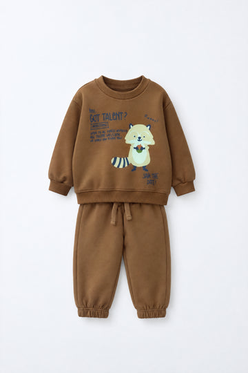Baby wearing a brown sweatshirt and jogger set with raccoon graphic, elasticated waistband and relaxed infant-friendly fit.