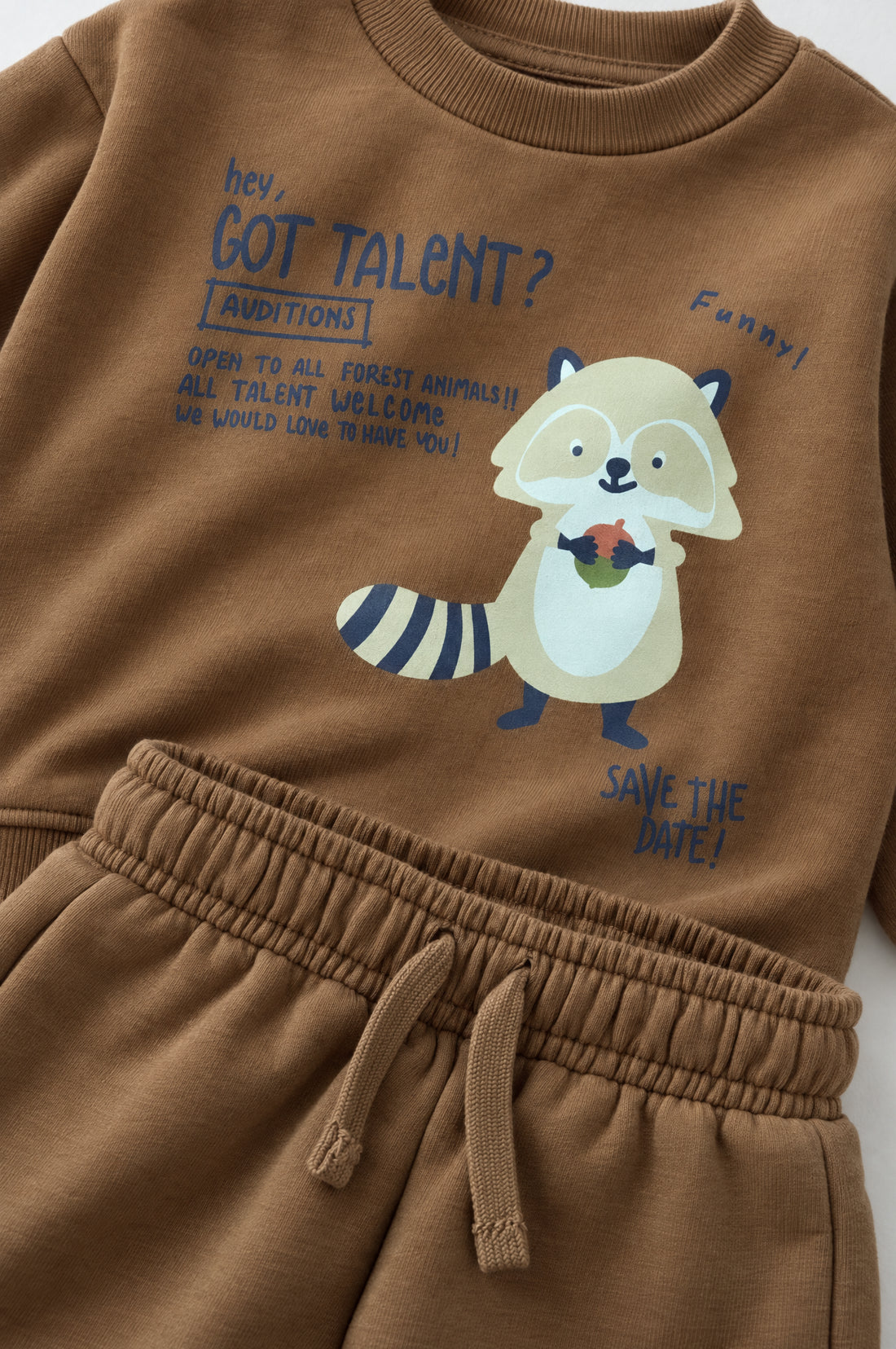 Baby wearing a brown sweatshirt and jogger set with raccoon graphic, elasticated waistband and relaxed infant-friendly fit.