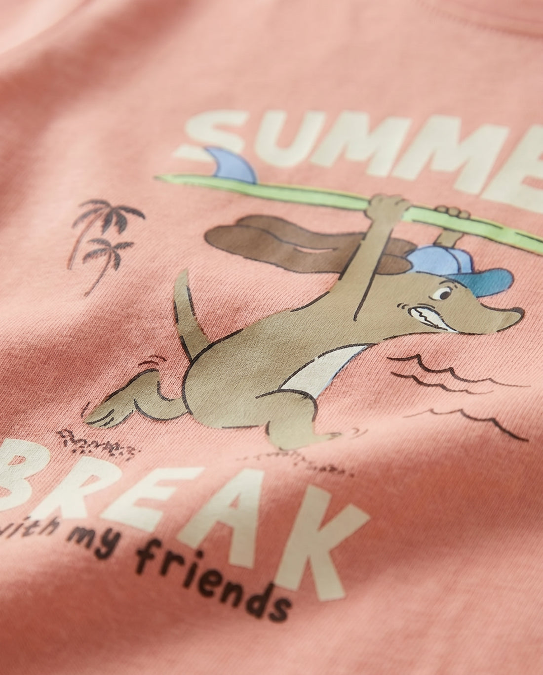 kid's salmon pink short sleeve cotton t-shirt with cartoon surfing animal, beach scene, and "Summer Break with my friends" graphic print on front, flat lay on light grey background
