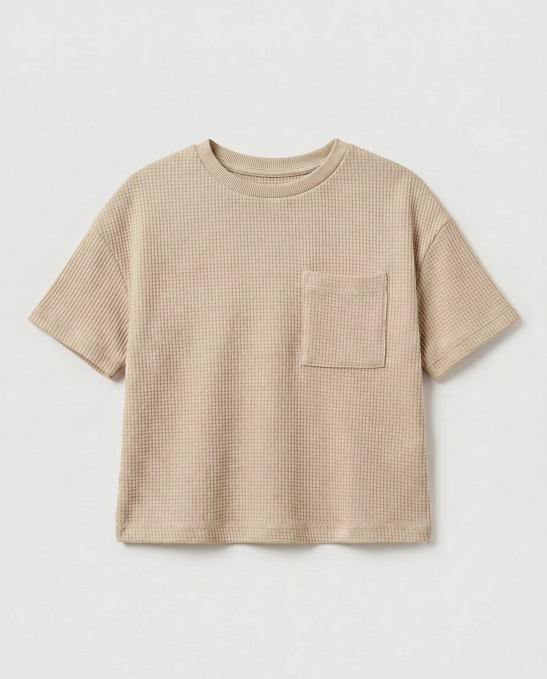 Full flat lay front view:
Kids' drop shoulder waffle cotton t-shirt in sand displayed flat lay on a white background, showing a relaxed boxy silhouette, ribbed crew neckline, short sleeves with ribbed cuffs, tonal chest patch pocket, and finished base hem.