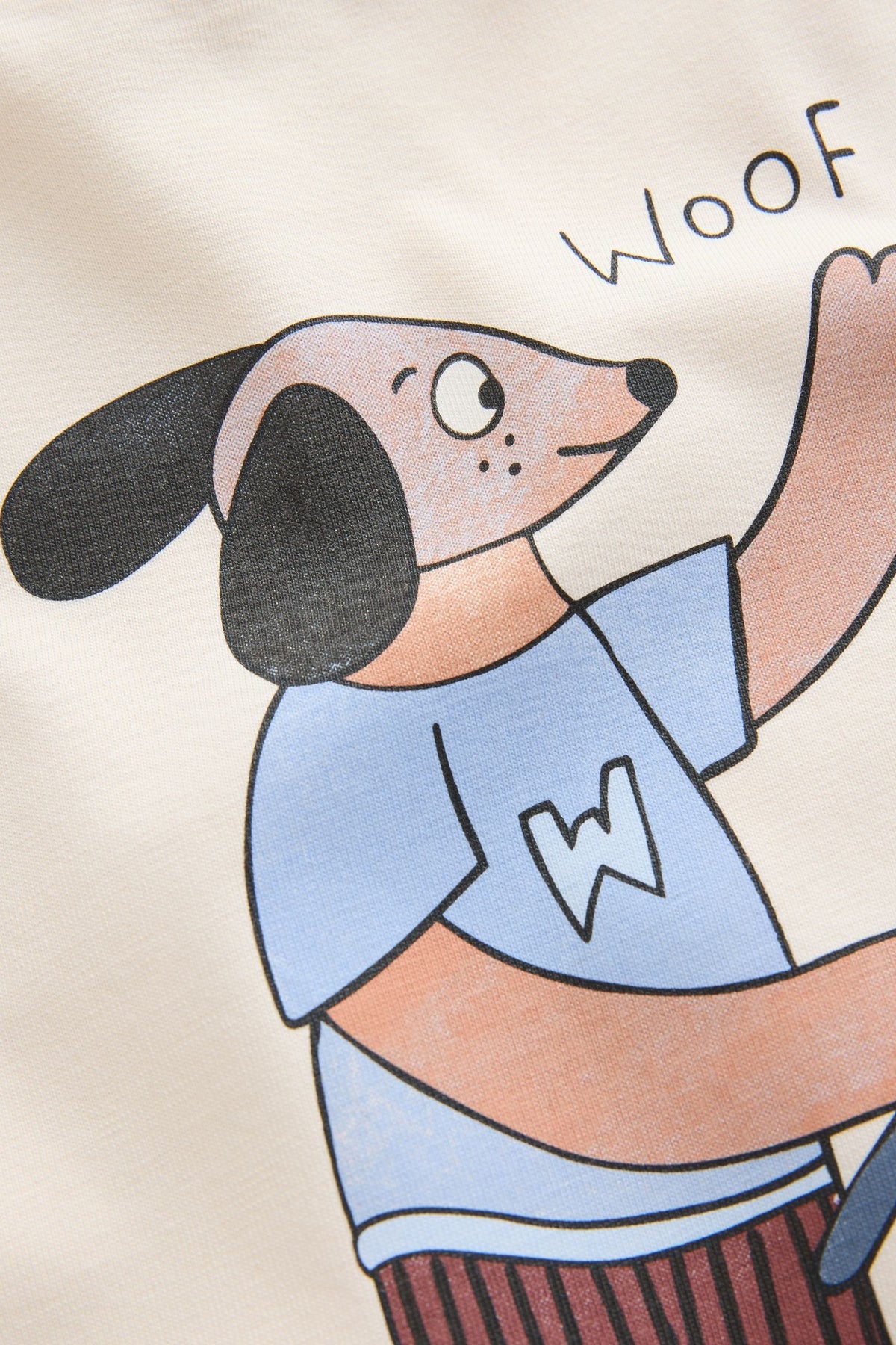 Close-up of the textured dog and “Woof” print on PTex Fashion cream long sleeve kids’ t-shirt