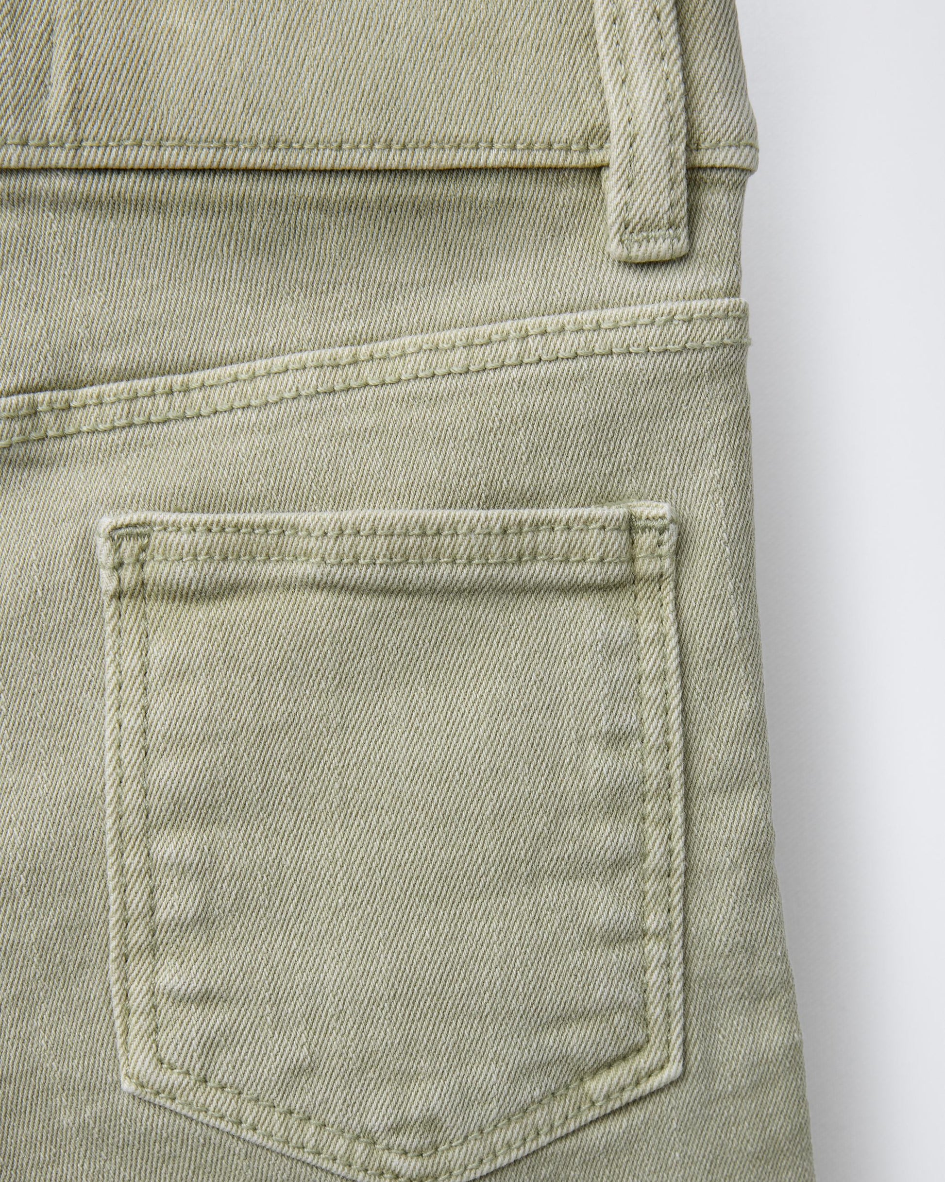Close-up of back patch pocket on sage green boys' denim Bermuda shorts, showing contrast topstitching detail and soft washed cotton denim texture.