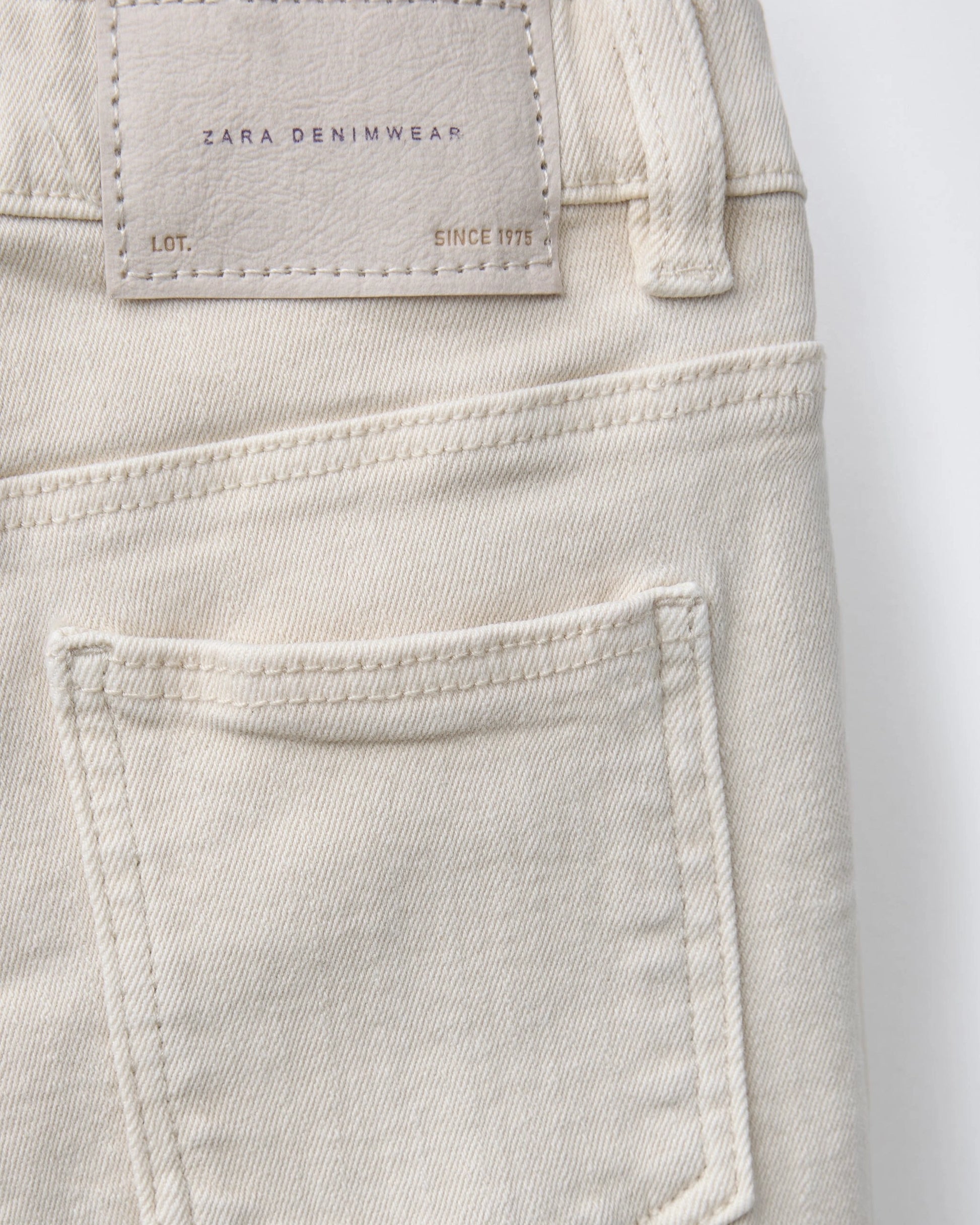 Back view detail of toddler denim Bermuda shorts featuring a structured back pocket and embossed leather brand patch on off-white denim.