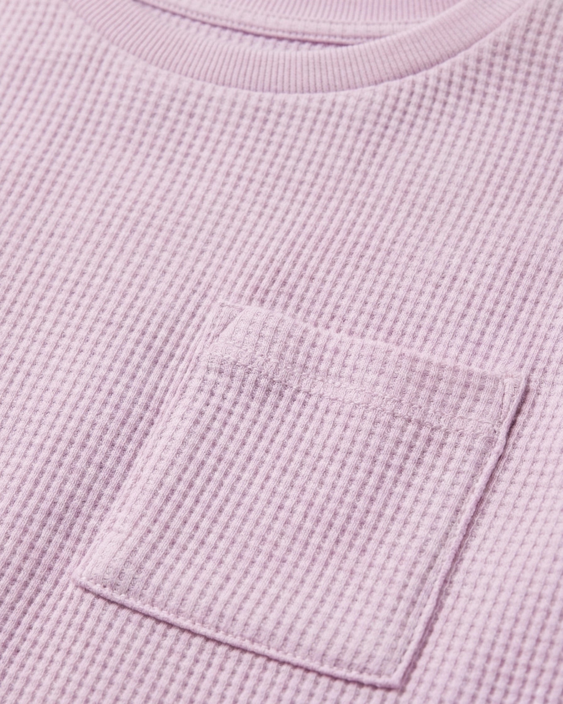 close up image of Toddler girls' waffle-knit cotton t-shirt in pink lilac with a ribbed crew neck, short sleeves, and a chest patch pocket, laid flat on a light grey background.
