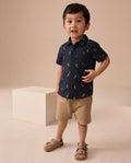 Child wearing a navy shirt with orange patterns and beige shorts on a beige background
